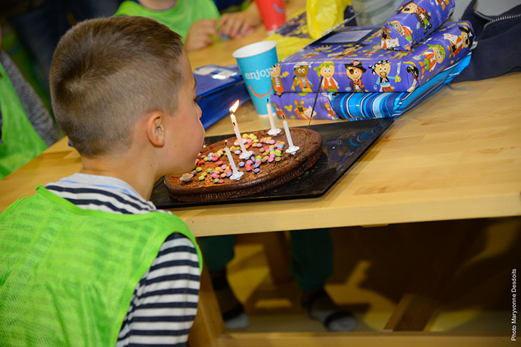 Un enfant souffle des bougies sur un gâteau d'anniversaire entouré de cadeaux